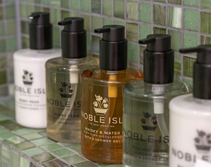 Five bottles of luxury products from Noble Isle are on shelf in the green-mosaic bathroom in a cabin at Fingal. 