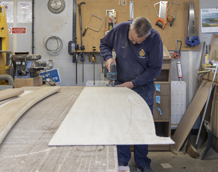 A Maintenance man is cutting out the template of wood. 