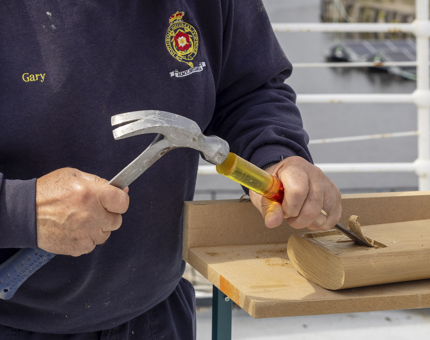 A man using a hammer and chisel on a wooden handrail. 