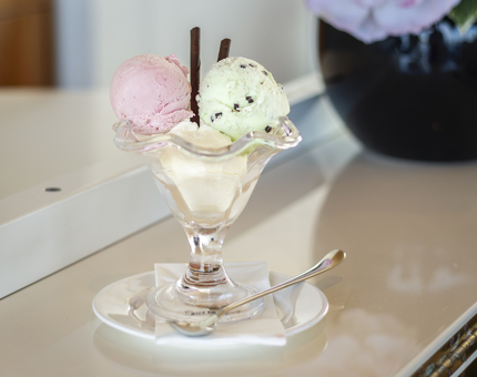 Three scoops of ice cream, strawberry, mint and vanilla, with a chocolate straw in a glass dish.