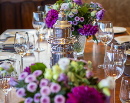 The dining table in Fingal's Bridge. There are pink and purple floral displays and and a silver lighthouse wine cooler.