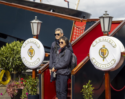 A man and a woman standing on the Royal Brown steps at The Royal Yacht Britannia. 