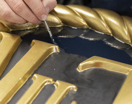 A closeup of a hand holding a paintbrush painting a sign. 