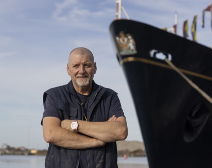 A man standing with with his arms crossed in front of a ship. 