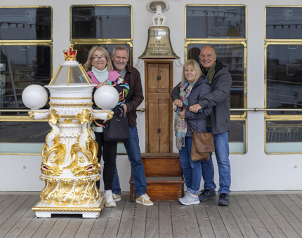 Four people pose by the bell and decorative compass binnacle. 