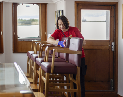 A woman in a red shirt wiping down four chairs. 