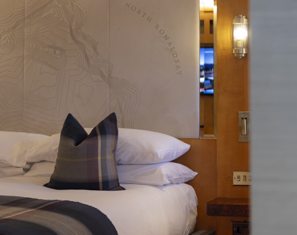 A detailed image of a bed's headboard with a tartan pillow and blanket. 