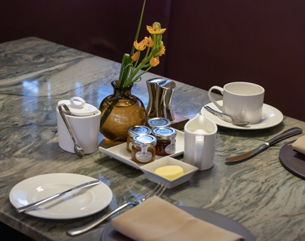 A table set with two place settings and a small brown vase with yellow flowers. 