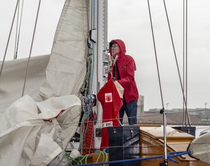 A man wearing a red jacket hoisting a sail on a yacht. 