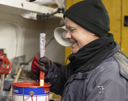 A man stirring a tin of red paint. 