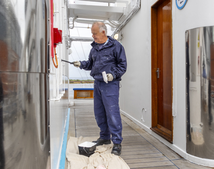 A man painting a wall of one of Britannia's decks white. 
