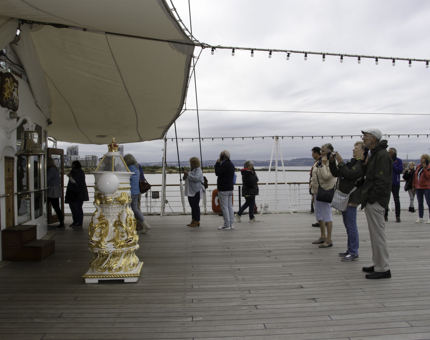 Visitors stand on outside deck of Britannia taking photographs of large ornate compass.
