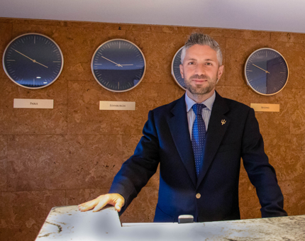 Man stands behind Reception desk at Fingal with world clocks on the wall in the background.