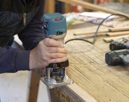 A close-up of a hand holding a hand saw cutting wooden beading. 