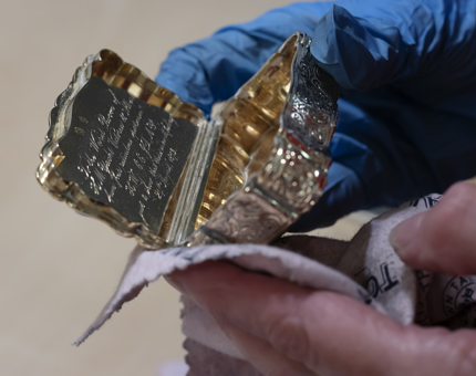 A close-up of a small silver box with engravings being polished. 