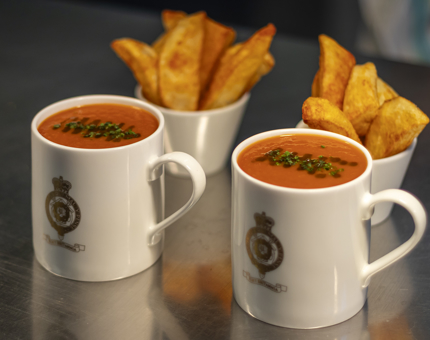 Two mugs of roasted red pepper and tomato soup and two bowls of potato wedges.