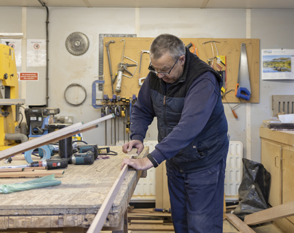 A man in a workshop sanding wooden beading. 