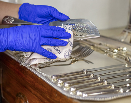 Hands wearing blue gloves polishing silver cutlery. 