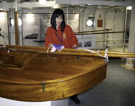 Housekeeper polishes the wood on the small sailing boat Tui which is on display in the Royal Sailing Exhibition.