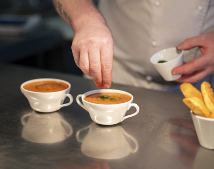 A chef preparing two bowls of soup and wedges.