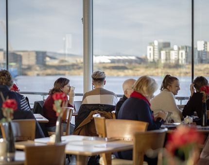 Visitors at tables in the Tearoom with views over the waterfront from the windows. 