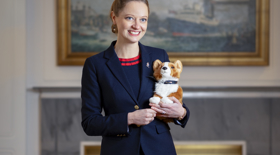 A woman standing in the Drawing Room holding a corgi plush toy. 