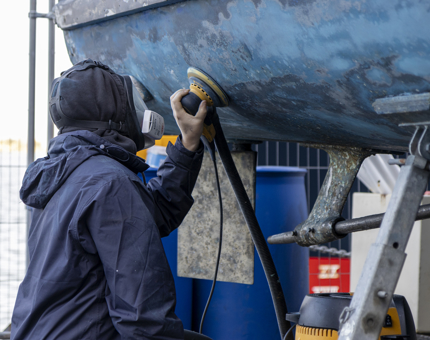 A Maintenance team member sanding a blue boat. 