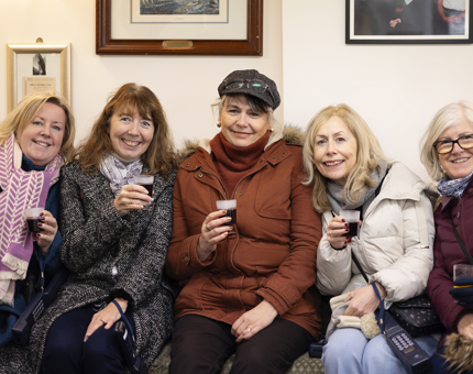 Five ladies sitting on a bench with glasses of mulled wine.
