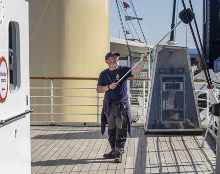 A Facilities Officer cleaning the Bridge with a long duster.