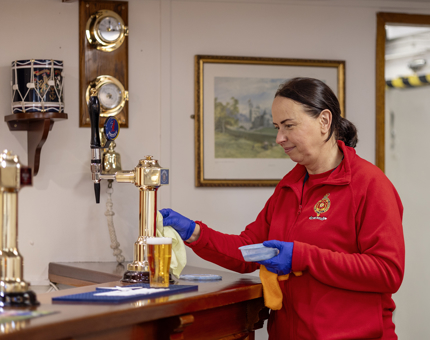 A member of the Housekeeping team cleaning brass taps in the Chief Petty Officer's Mess. 