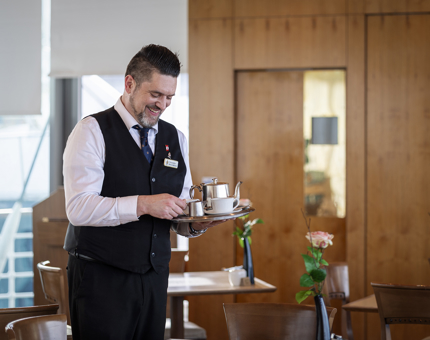 A member of the Tearoom team carrying a tray with a teapot and cup on it.
