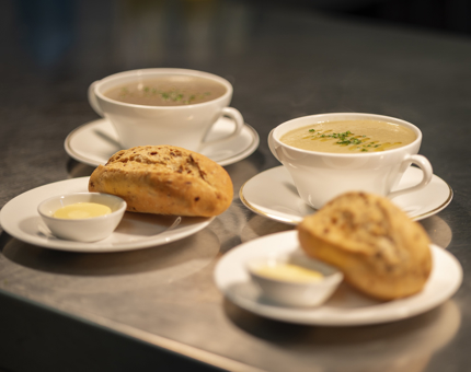 Two bowls of soup with two plates of bread and butter.
