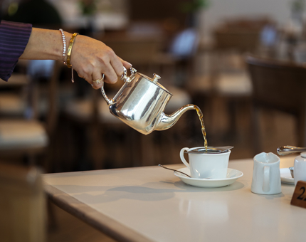 A hand holding a silver pot, poring tea into a white teacup.