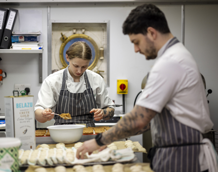 Two Chefs in the Galley preparing cheesecake bases and bread rolls for an evening event.