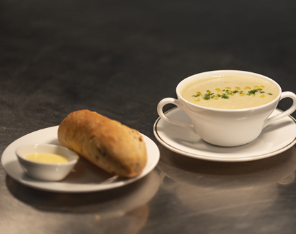 A bowl of Cullen skink soup with a plate containing a brown bread roll and pot of butter. 