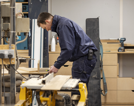 In the Joiner's Workshop, a man measures wood to make drawers for on board storage. 