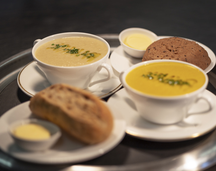 A tray with two bowls of soup and two bread rolls and butter.