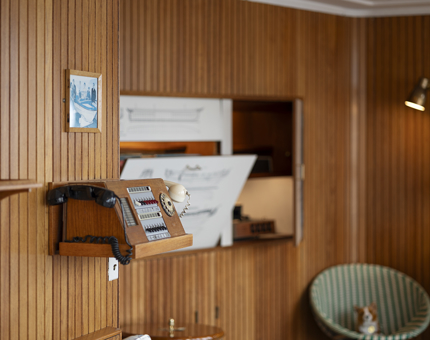 A section of the teak-lined Sun Lounge. There is a phone on the wall and a round green chair with a corgi plush toy on it.