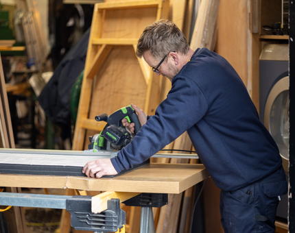 A man in the Joiners' Workshop cutting sound insulation on a bench. 