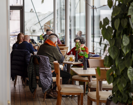 Guests sitting at tables in the Royal Deck Tearoom. There is a green plant in the foreground.