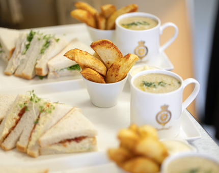 Plates of food ready to be served. They contain mugs of Cullen skink soup, bowls of potato wedges and sandwiches.