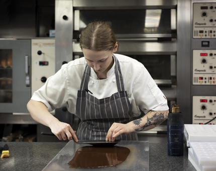 Senior Chef de Partie preparing vegan chocolate to be served at an evening event. Behind her are ovens.