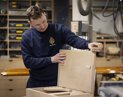 A fold down desk being made. The man making it is sanding the edges. 