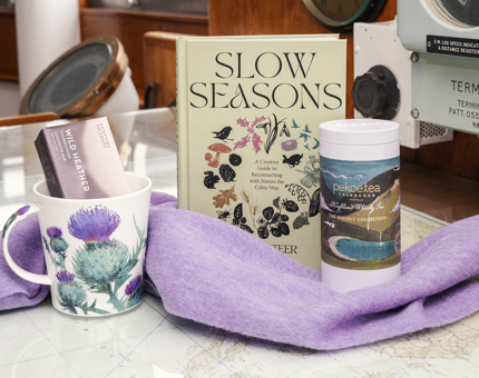 A purple scarf, mug, cannister of tea and a book are displayed together on a table. 