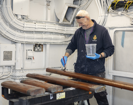A Maintenance man holding a tub of varnish and a paint brush. He is varnishing wooden handrails. 