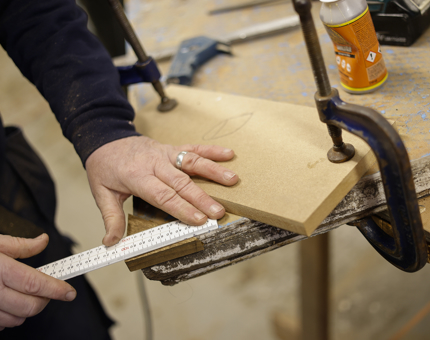A close up of a hand measuring a piece of wood. 
