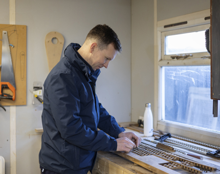 A maintenance man is standing at a workbench adding lattice details to a scupper board. 