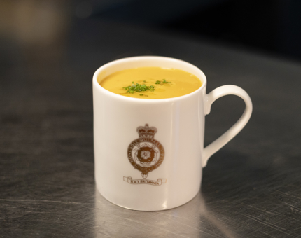 A white mug with a gold Britannia crest on it containing lentil soup. 