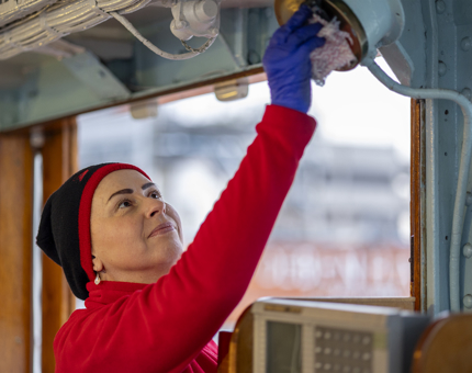 A Housekeeper is dusting equipment inside the Bridge. 