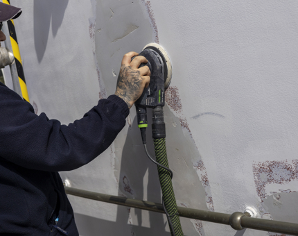  A Maintenance team member sanding the white paint off of a wall. 